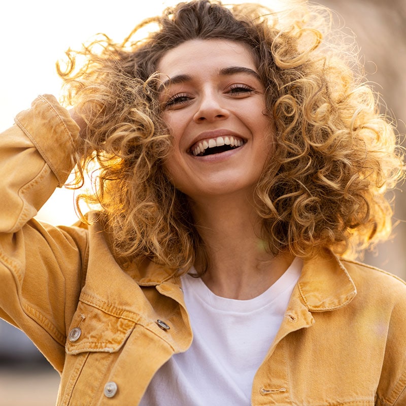 smiling woman with curly brown-blonde hair wearing yellow jean jacket