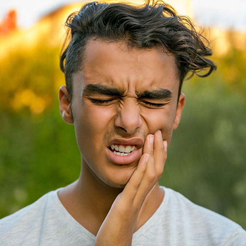 teen boy holding the side of his mouth in pain