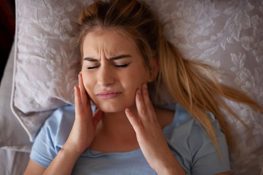 woman lying in bed holding jaw in pain