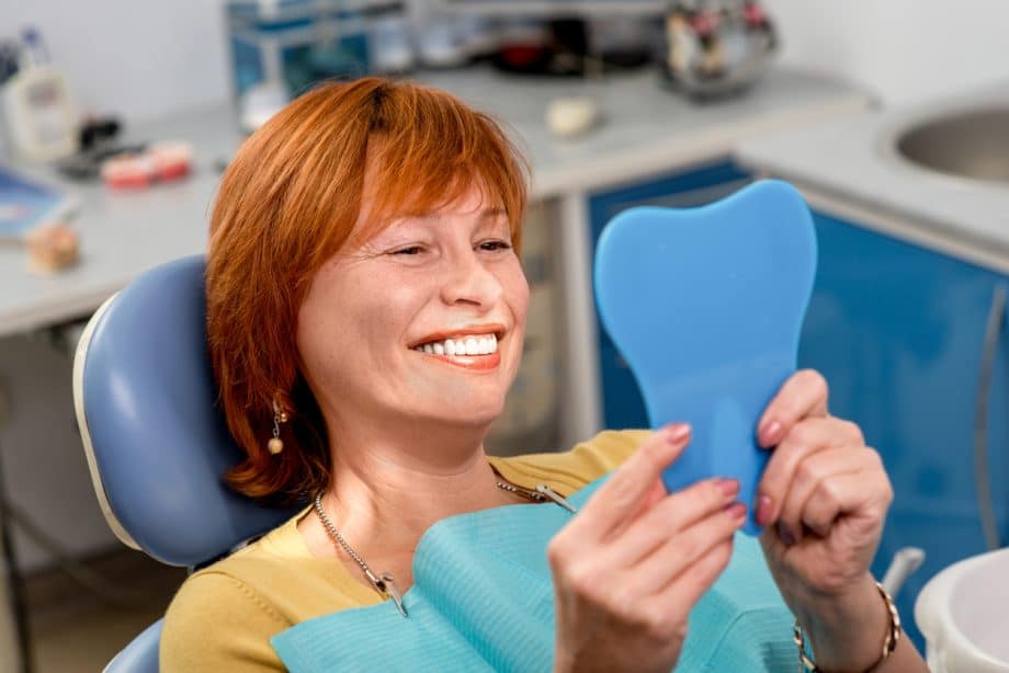 red-headed woman in exam chair holding mirror and smiling