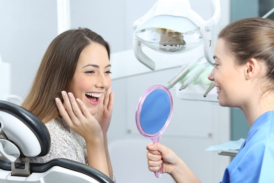 dental assistant holding up mirror for female dental patient